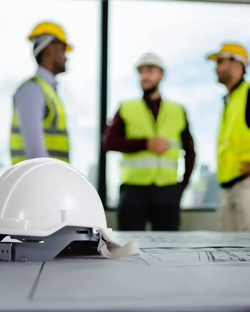 Office setup with safety helmet and team of electricians planning electrical and IT infrastructure.